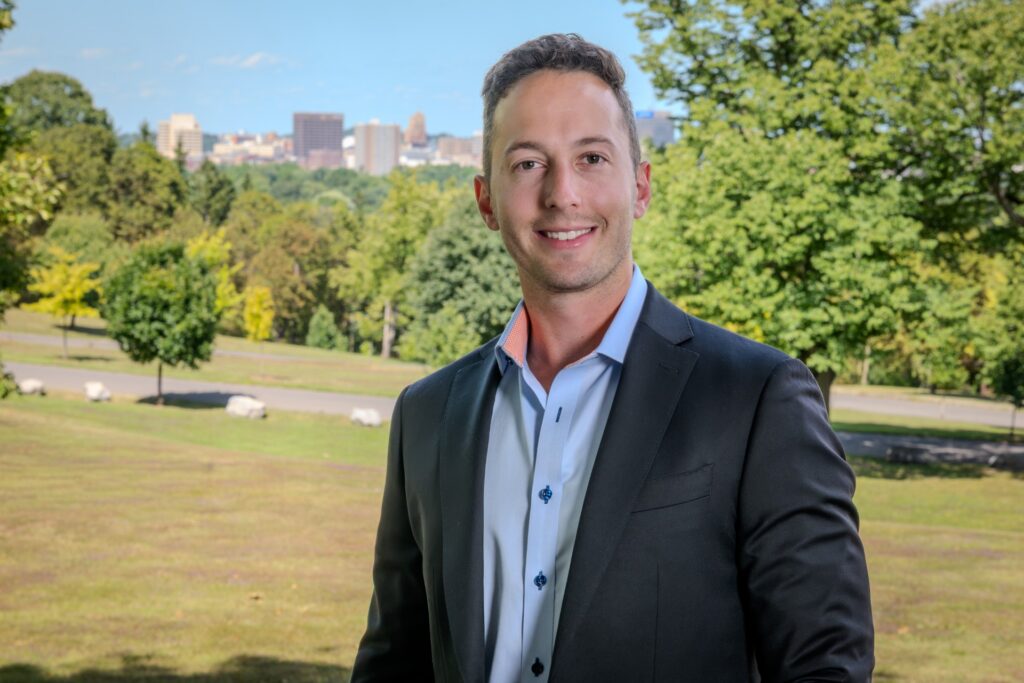 Angelo Niforatos, Vigilare AI CEO, outdoors with the Syracuse skyline behind him