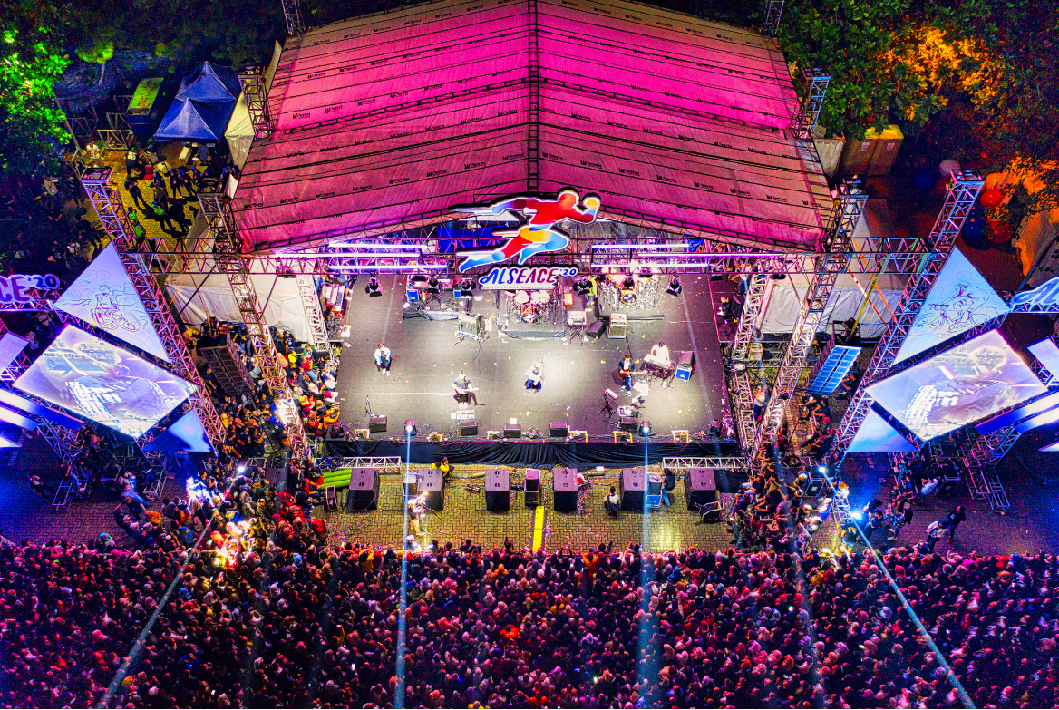 Aerial view of a concert stage and crowd illuminated by colorful lights